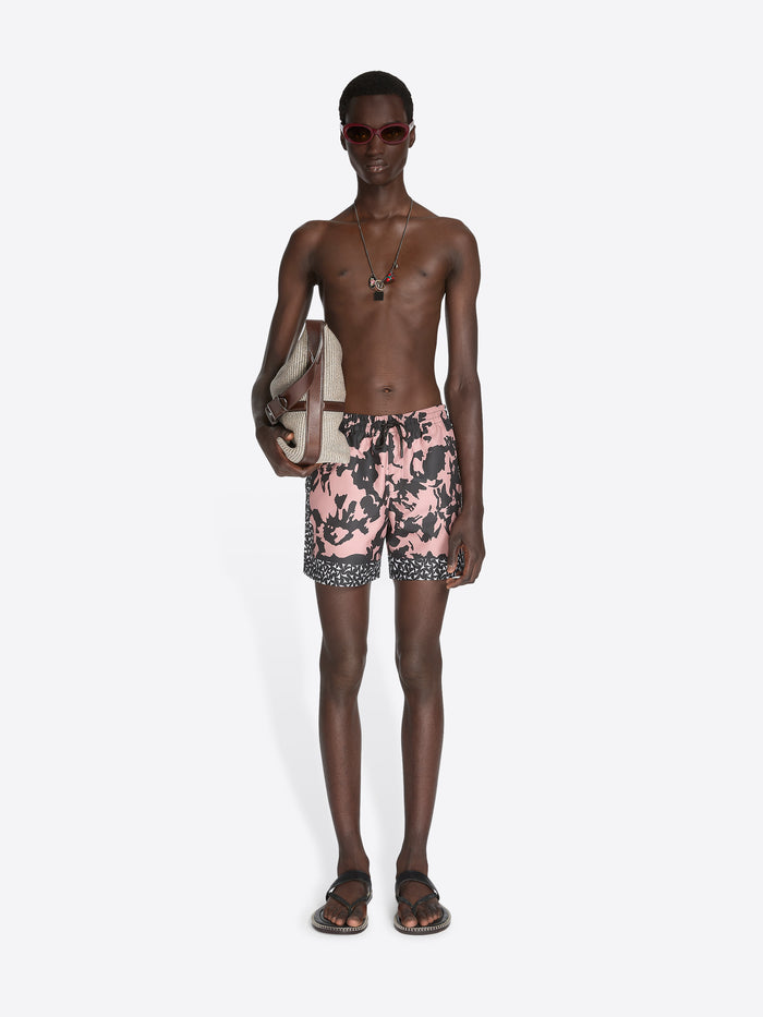 Man wearing pink floral swim shorts on a white background