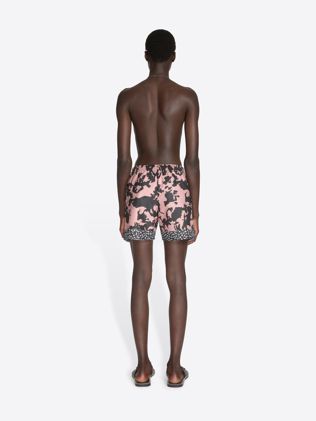Person wearing pink and black patterned swim shorts on a white background