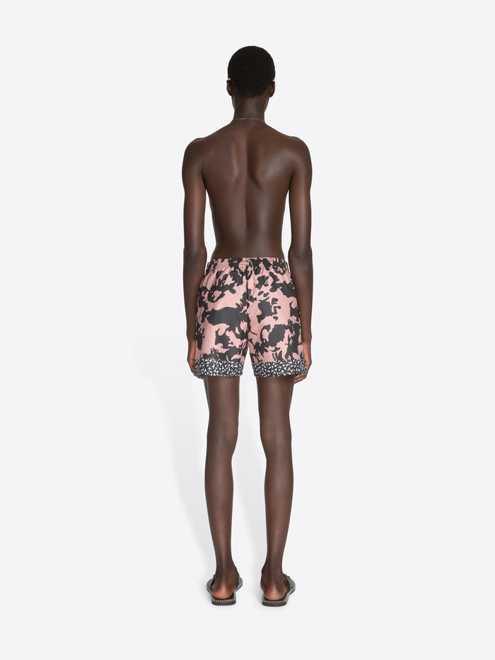 Person wearing pink and black patterned swim shorts on a white background
