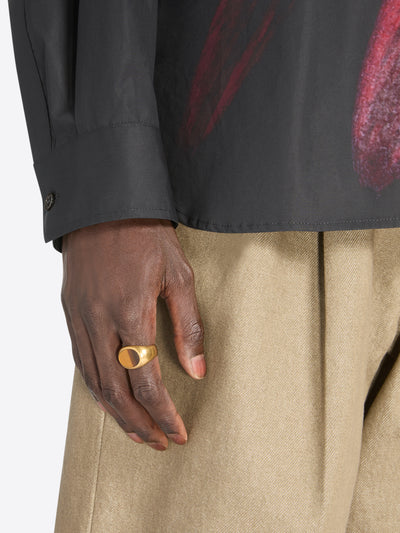 Hand wearing a gold ring with a dark background - Dries Van Noten