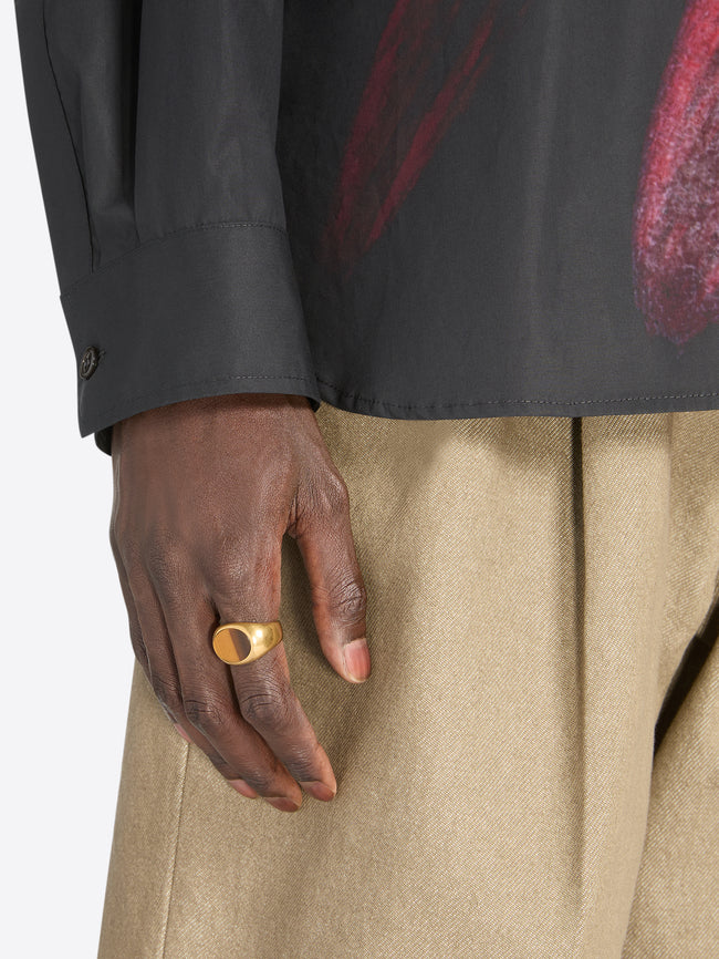 Hand wearing a gold ring with a dark background - Dries Van Noten