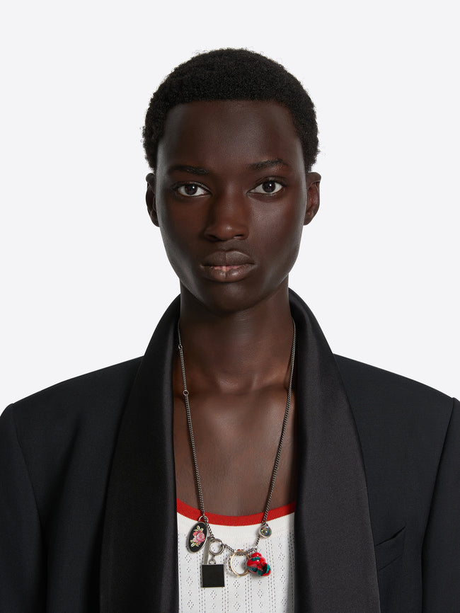 Person wearing a black blazer with a necklace featuring multiple pendants on a white background