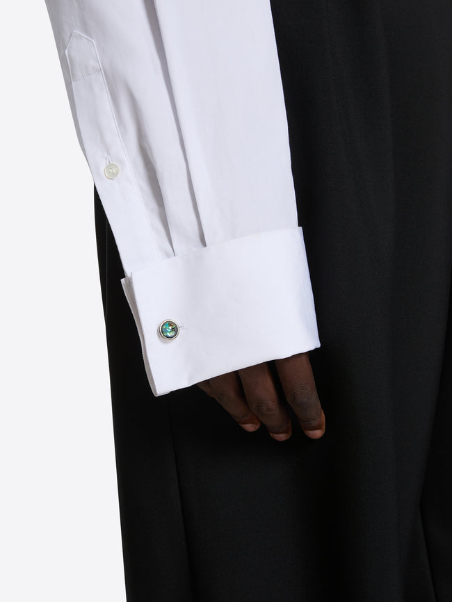 Close-up of a white shirt cuff with a green button on a black background