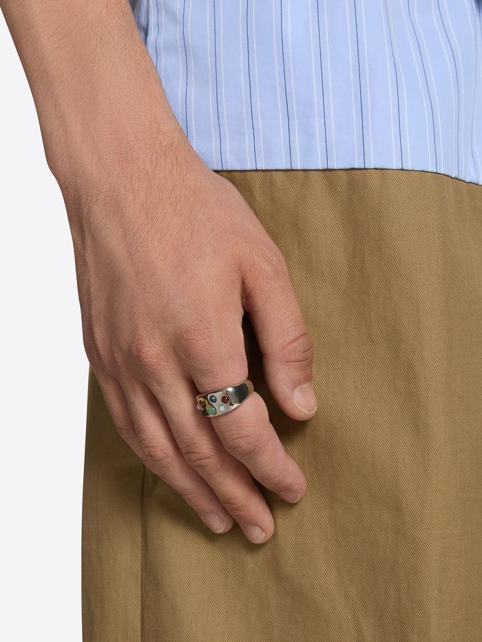 Hand wearing a ring with a light blue shirt and brown pants on a white background