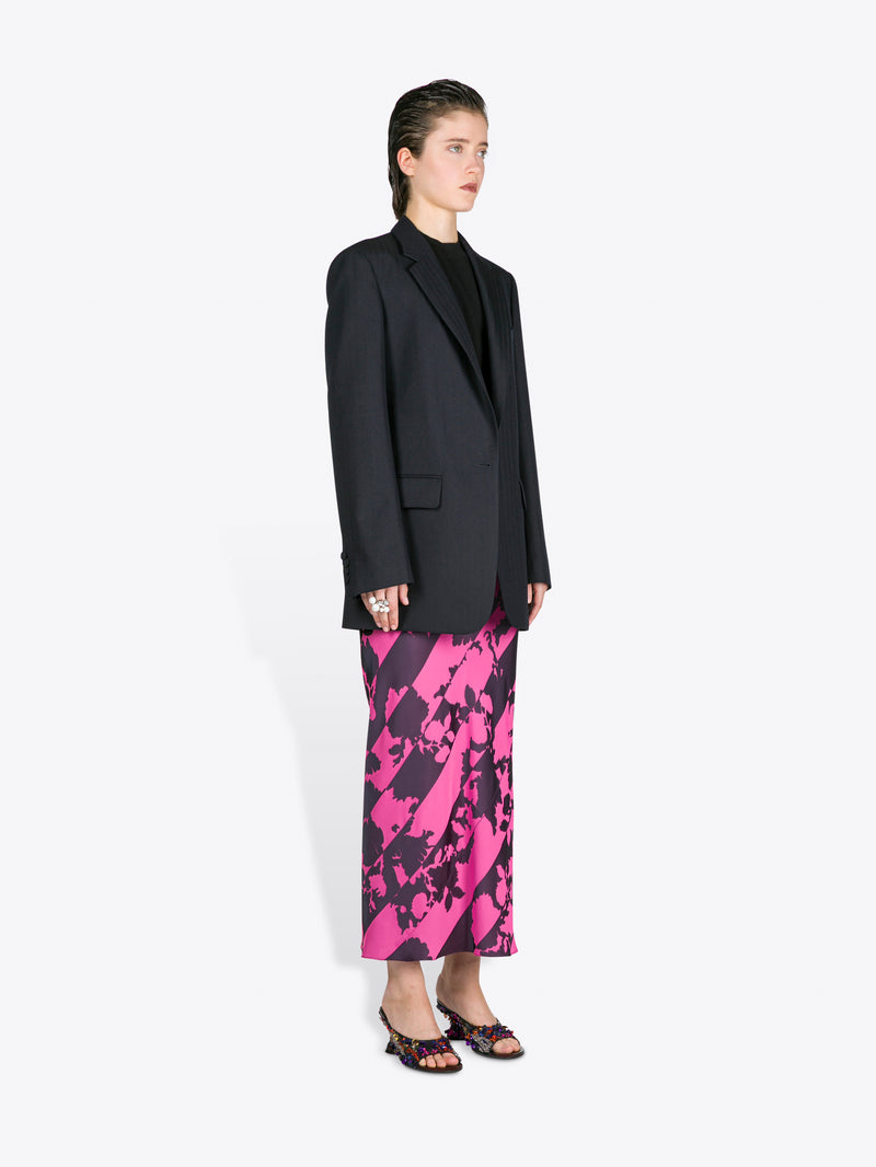 Person wearing a black blazer and pink and black patterned skirt on a white background - Dries Van Noten