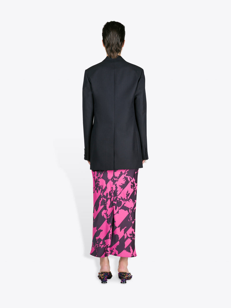 Person wearing a black blazer and pink and purple patterned skirt on a white background - Dries Van Noten