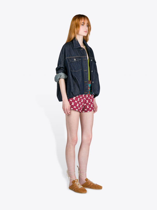 Woman wearing a denim jacket, patterned shorts, and brown shoes on a white background