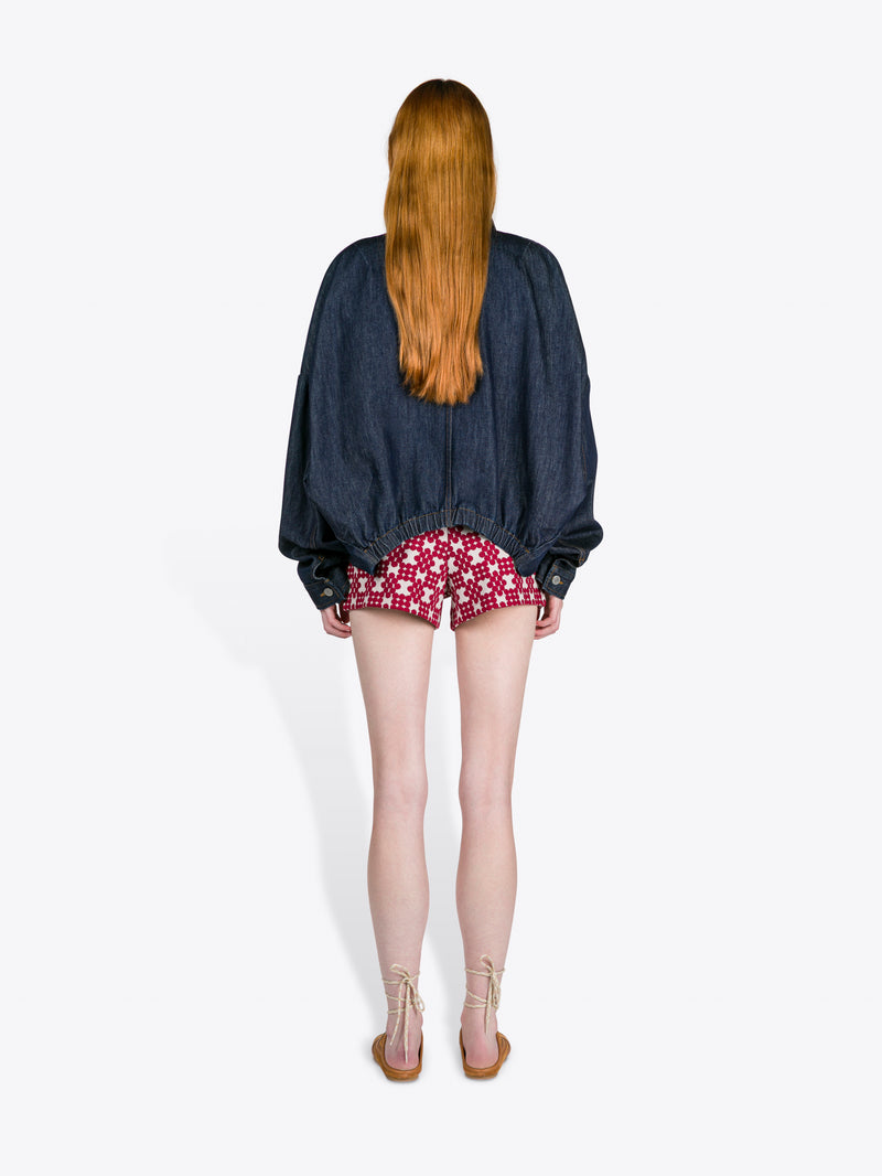 Person wearing a denim jacket and red patterned shorts on a white background