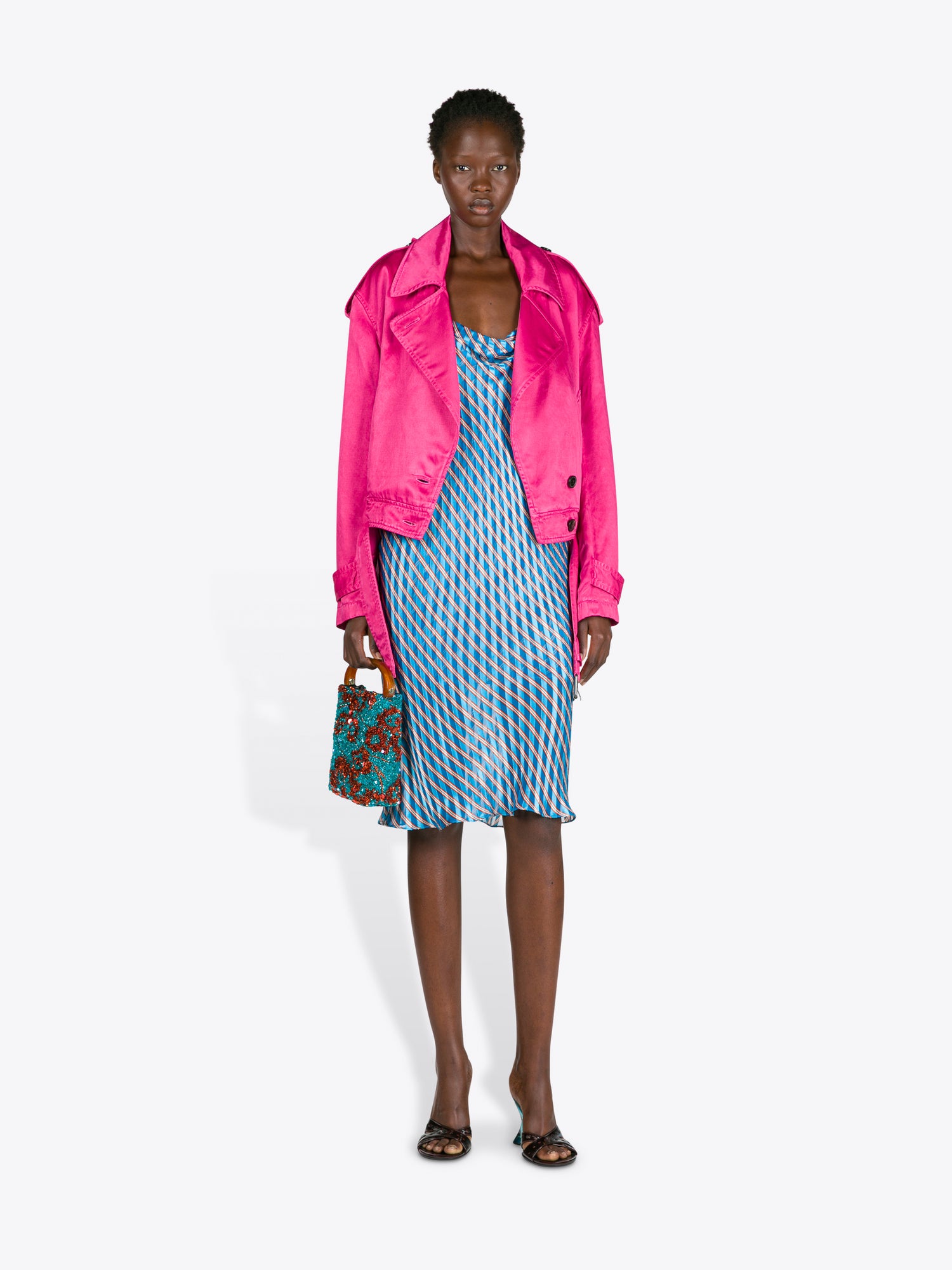 Woman wearing a bright pink jacket over a blue dress with a patterned handbag on a white background - Dries Van Noten