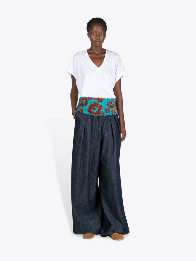 Woman wearing a white top and dark blue wide-leg pants with a colorful belt on a white background