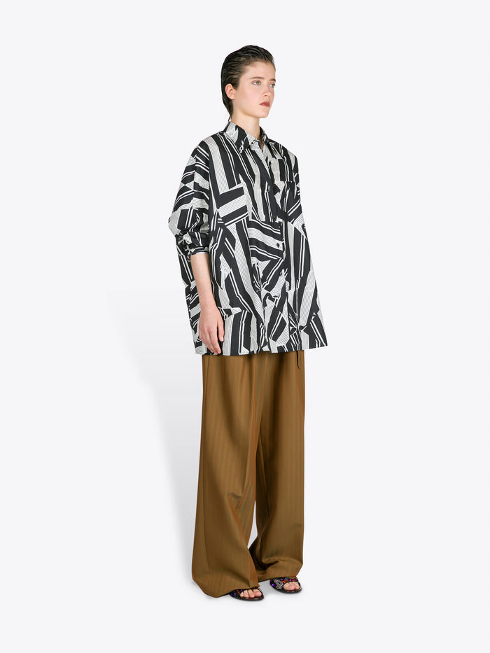 Person wearing a black and white patterned shirt with brown pants on a white background