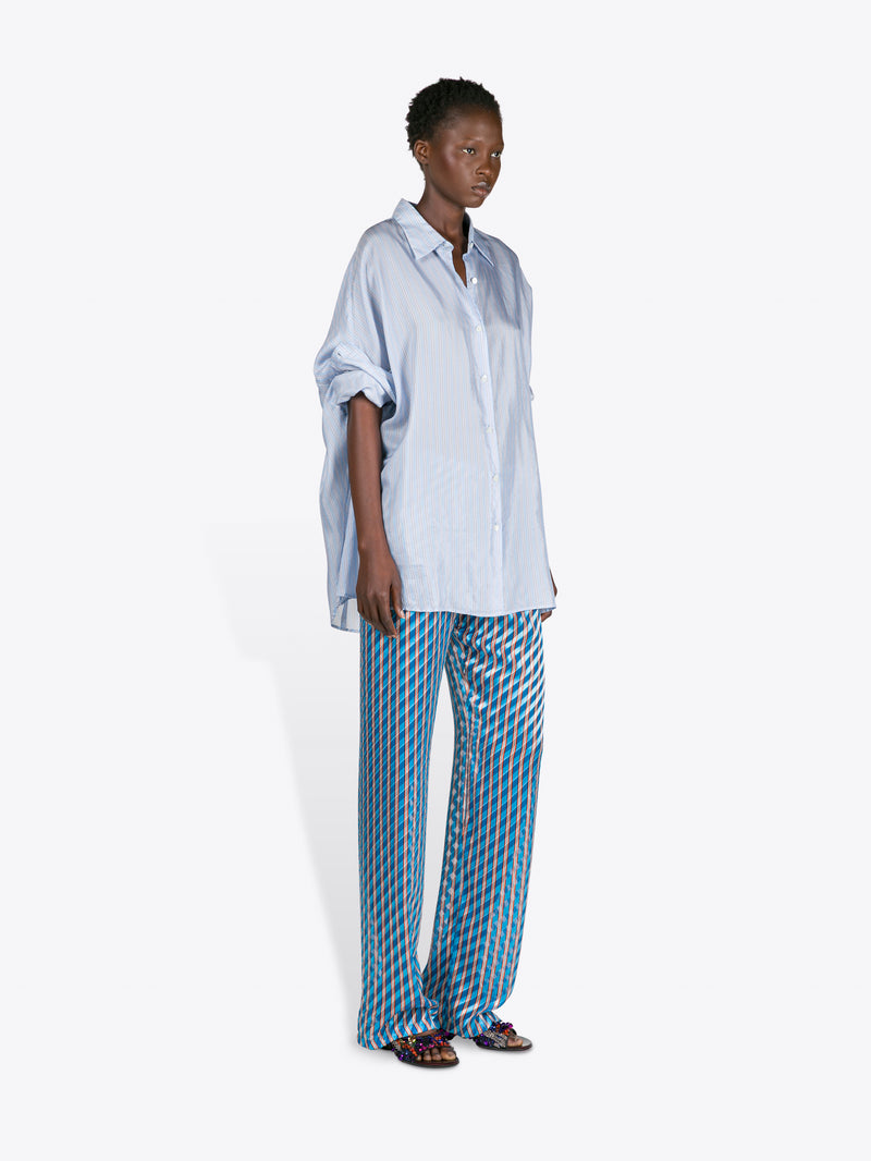Person wearing a light blue oversized shirt and blue checkered pants on a white background