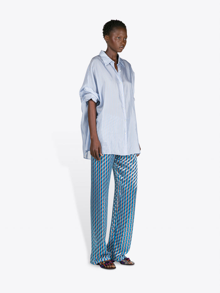 Person wearing a light blue oversized shirt and blue checkered pants on a white background