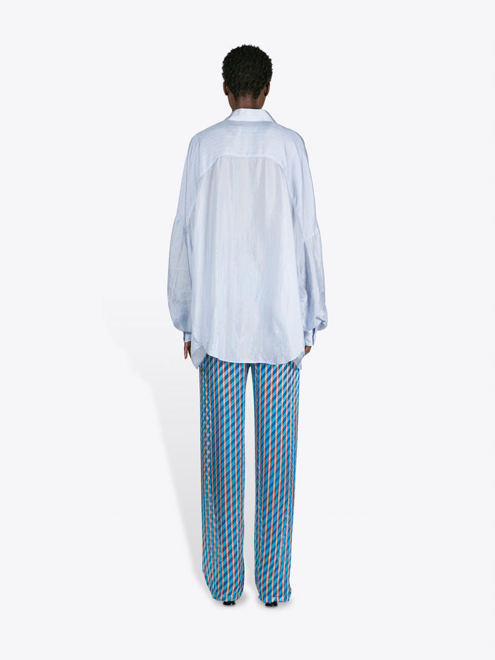 Person wearing a light blue shirt and patterned pants on a white background