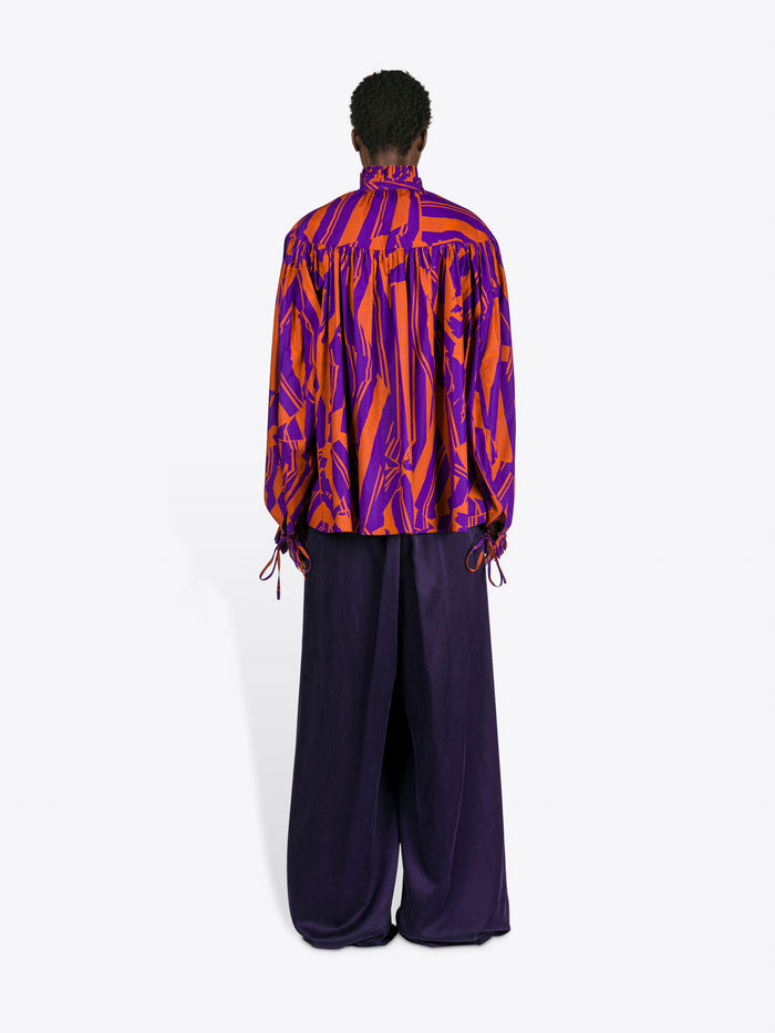 Person wearing a vibrant, patterned shirt and dark pants on a white background