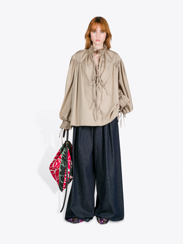 Woman wearing a beige blouse and dark pants, holding a colorful bag on a white background