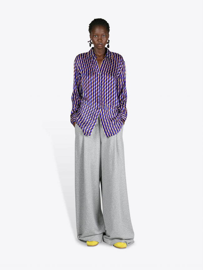Person wearing a purple checkered shirt and grey pants on a white background