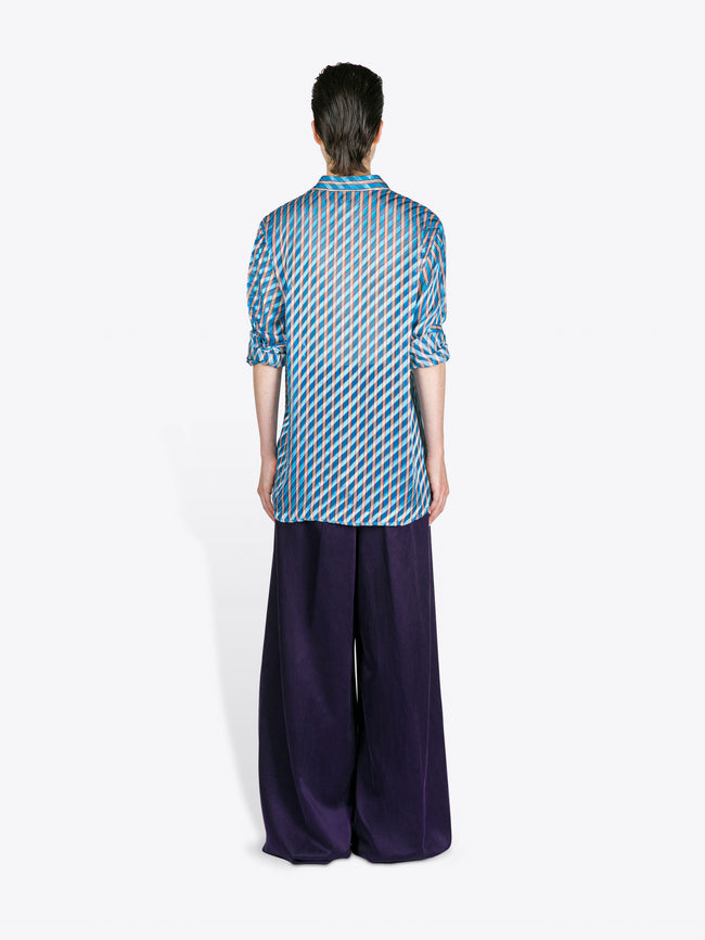 Person wearing a blue patterned shirt and dark pants on a white background