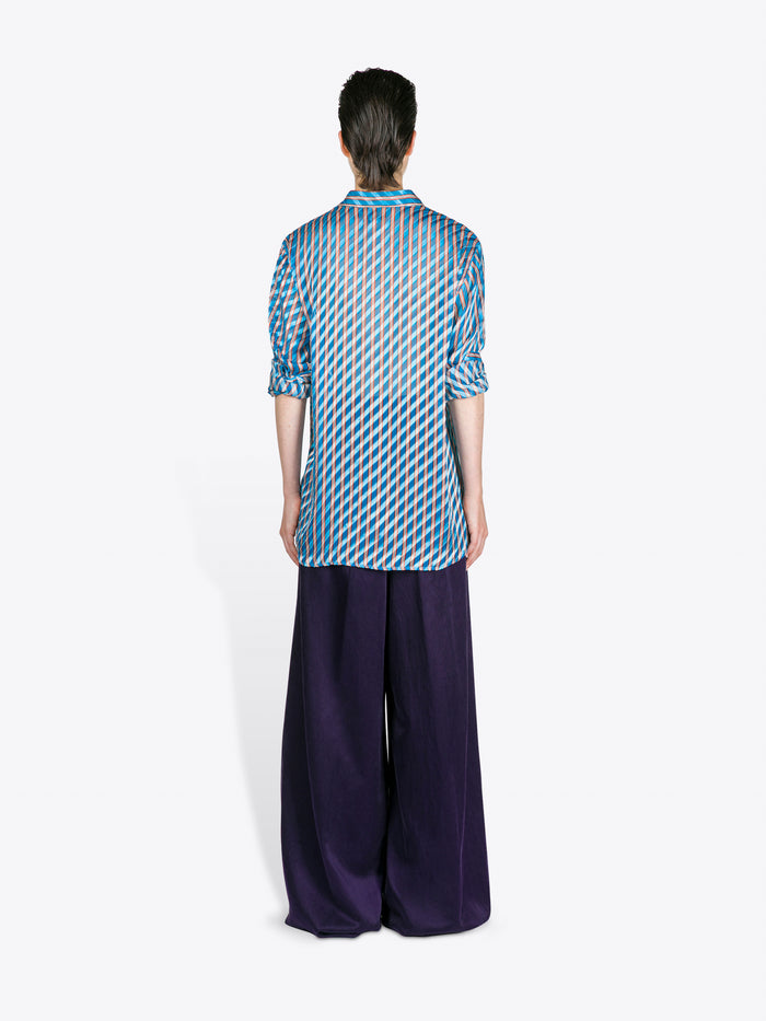 Person wearing a blue patterned shirt and dark pants on a white background