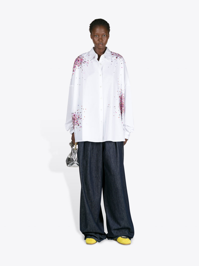 Person wearing a white shirt with floral patterns and dark pants on a white background
