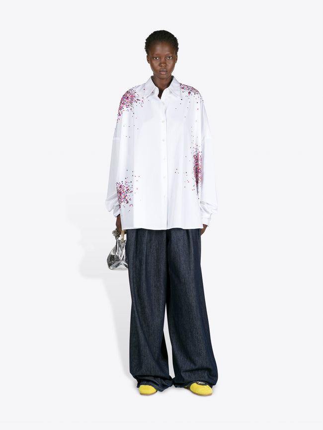 Person wearing a white shirt with floral patterns and dark pants on a white background