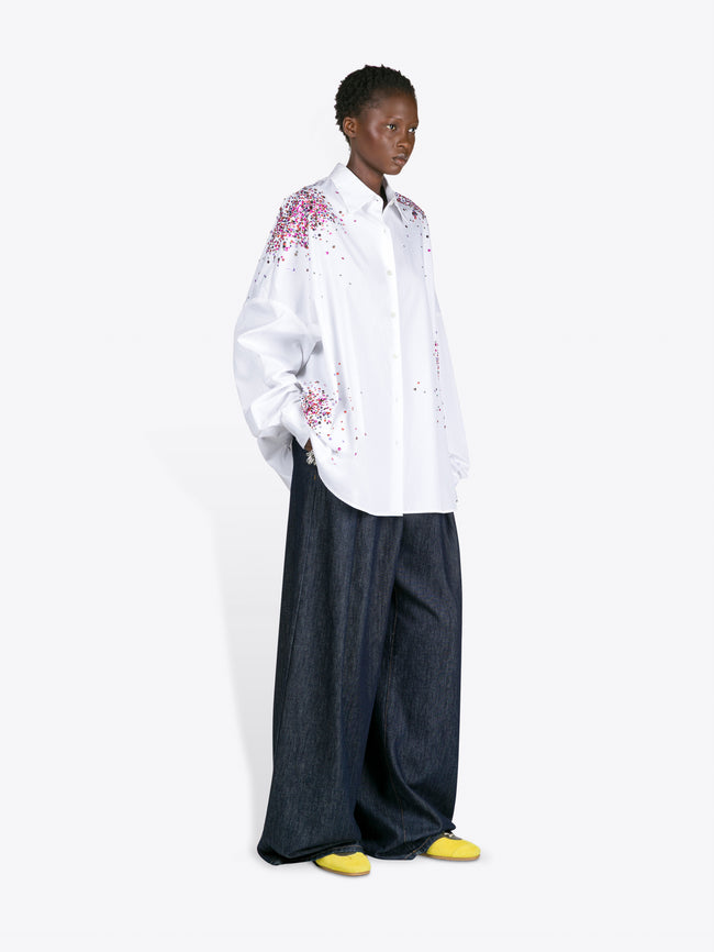 Person wearing a white embroidered shirt and dark pants on a white background