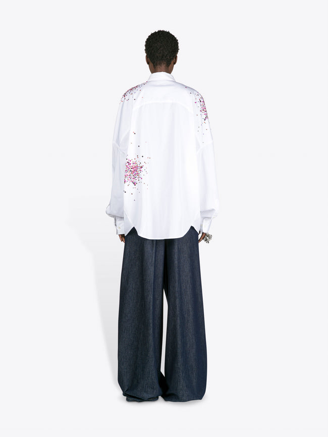 Person wearing a white embroidered shirt and dark pants on a white background