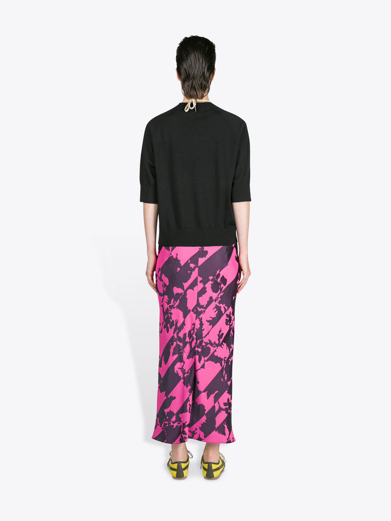 Person wearing a black top and pink and purple patterned skirt on a white background