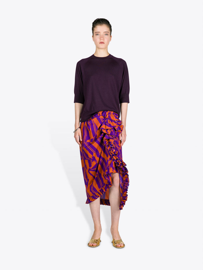 Woman wearing a dark purple top and patterned skirt on a white background