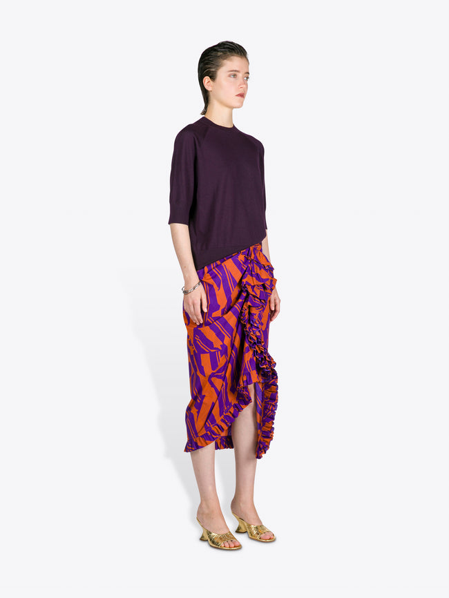 Woman wearing a dark purple top and colorful patterned skirt on a white background