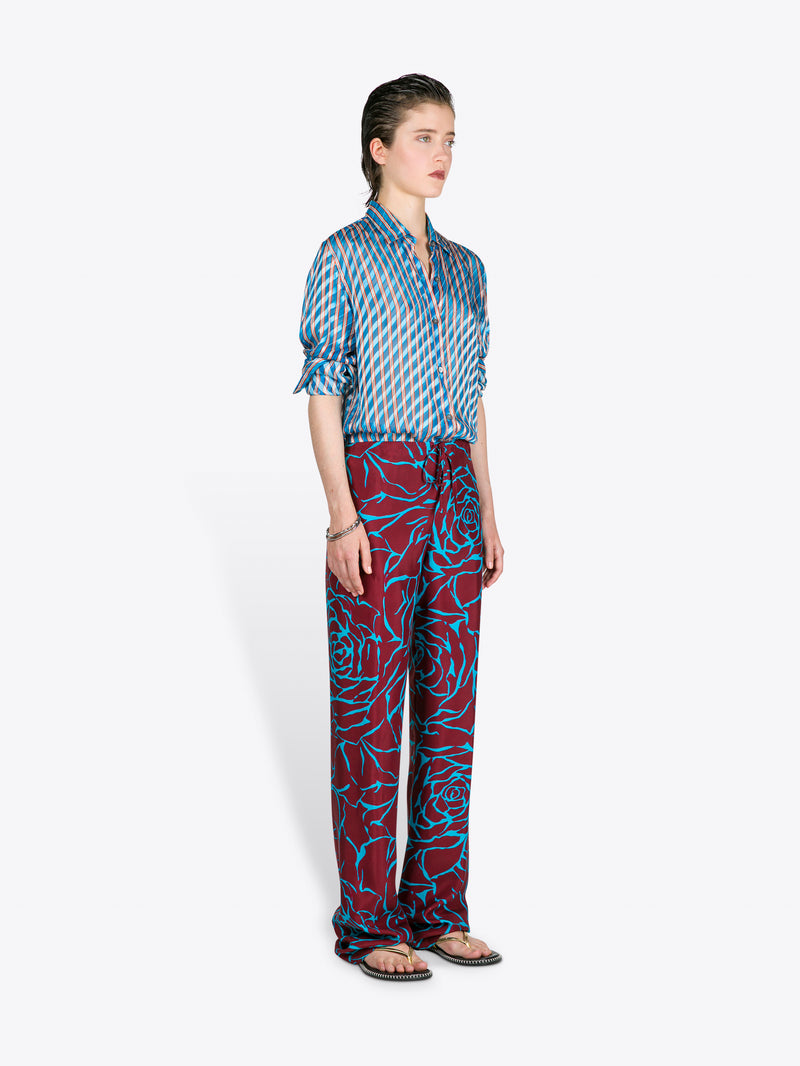 Person wearing a blue patterned shirt and red patterned pants on a white background