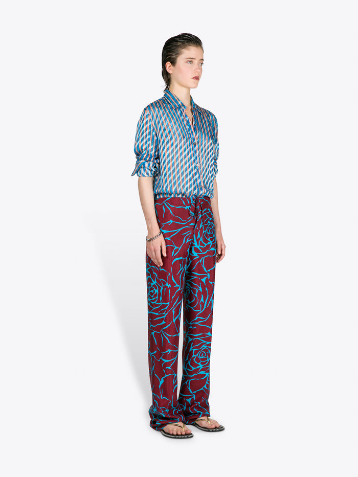 Person wearing a blue patterned shirt and red patterned pants on a white background