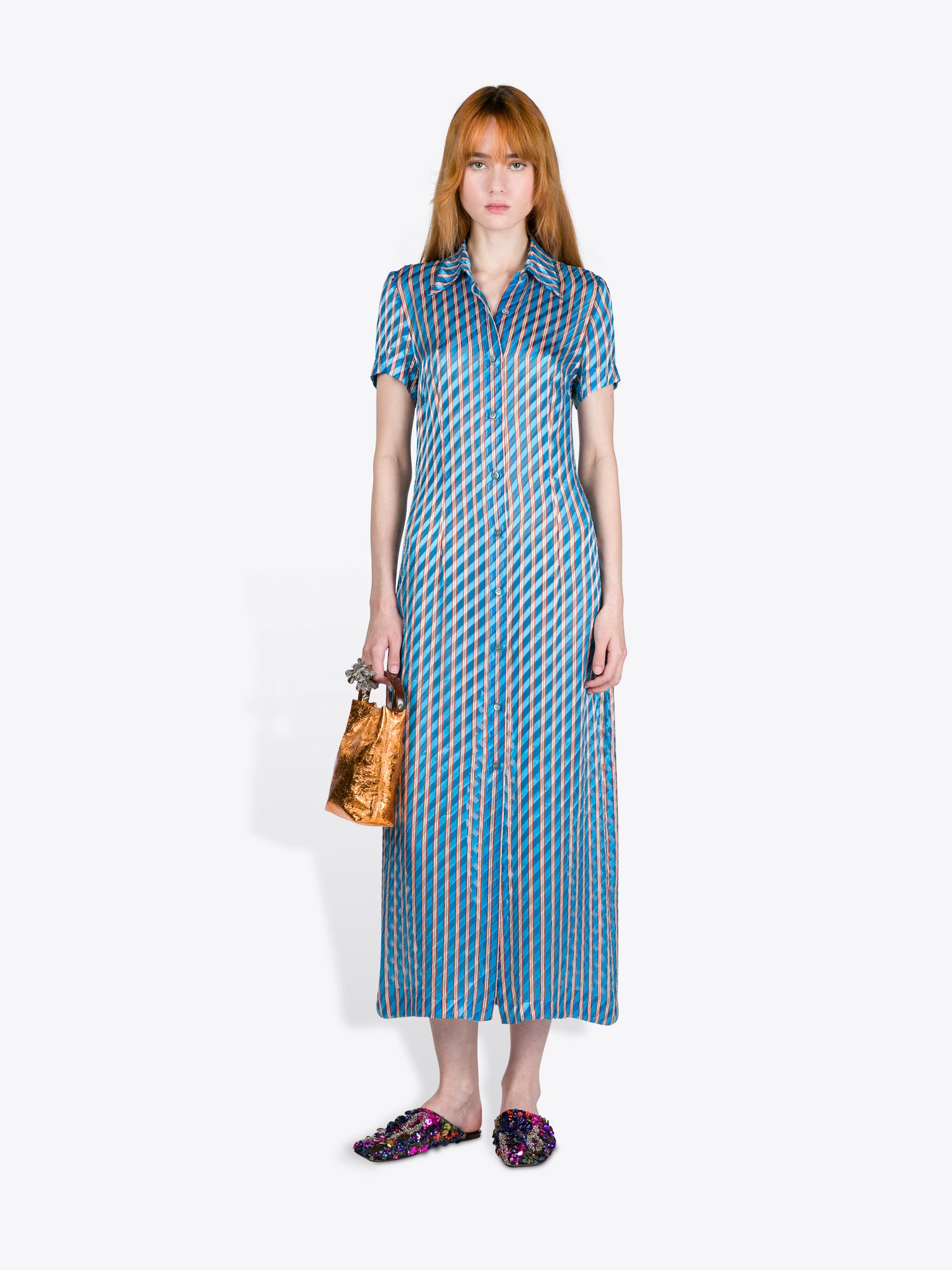 Woman wearing a blue patterned dress holding a gold handbag on a white background - Dries Van Noten