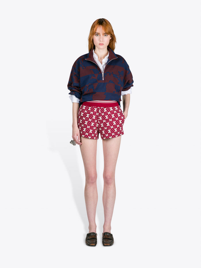 Person wearing a navy patterned sweater and red shorts with white star design on a white background - Dries Van Noten