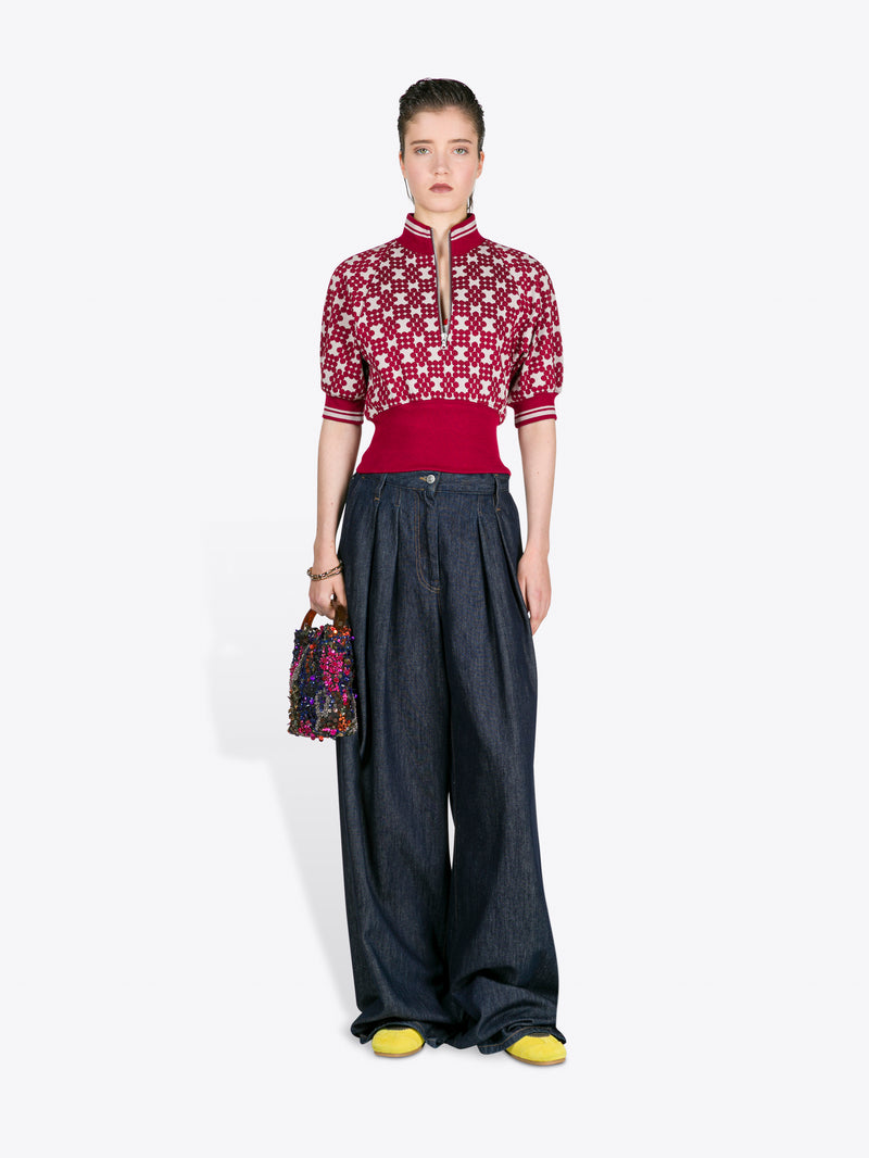 Woman wearing a red and white patterned top with dark pants, holding a colorful bag on a white background - Dries Van Noten