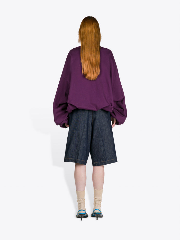 Person wearing a purple shirt and dark shorts from behind on a white background