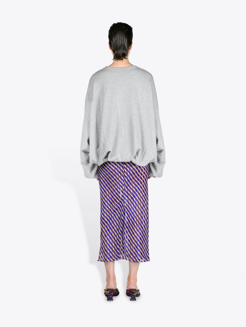 Person wearing a gray sweater and purple patterned skirt on a white background