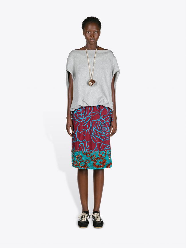 Model wearing a gray top and colorful patterned skirt on a white background