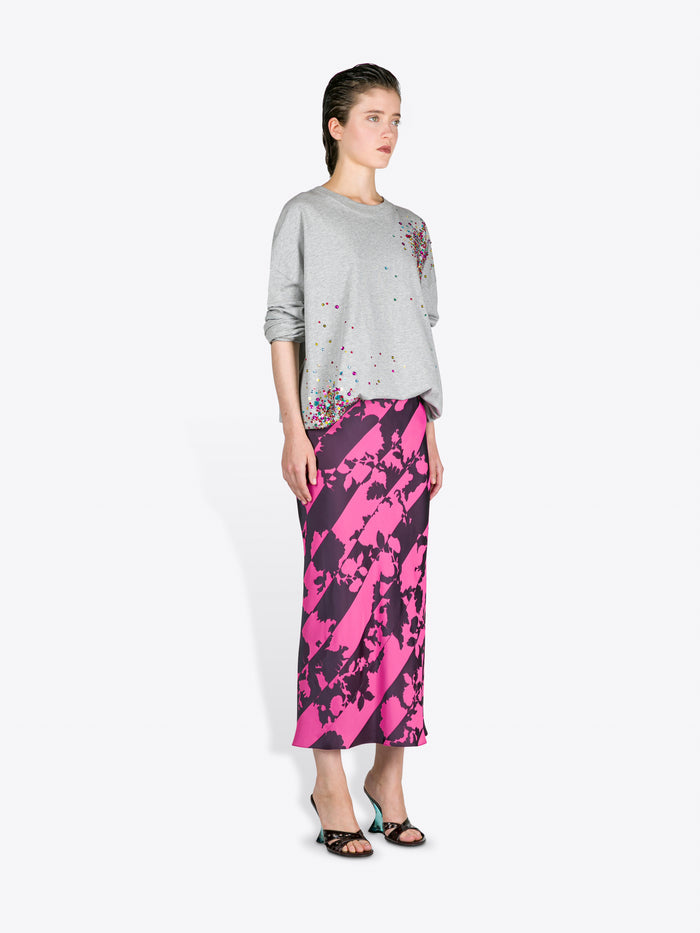 Woman wearing a grey sweater with floral design and a pink and black patterned skirt on a white background