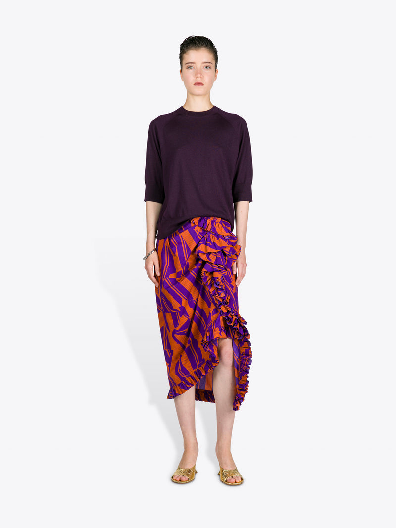 Woman wearing a dark purple top and patterned skirt on a white background
