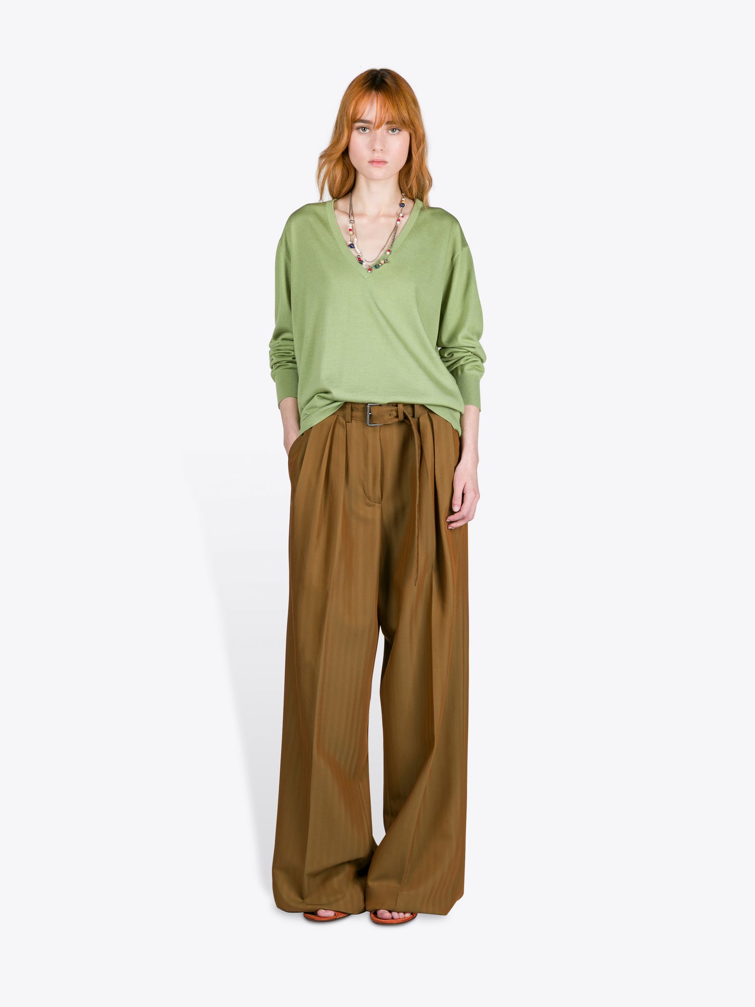 Woman wearing a green top and brown wide-leg pants on a white background