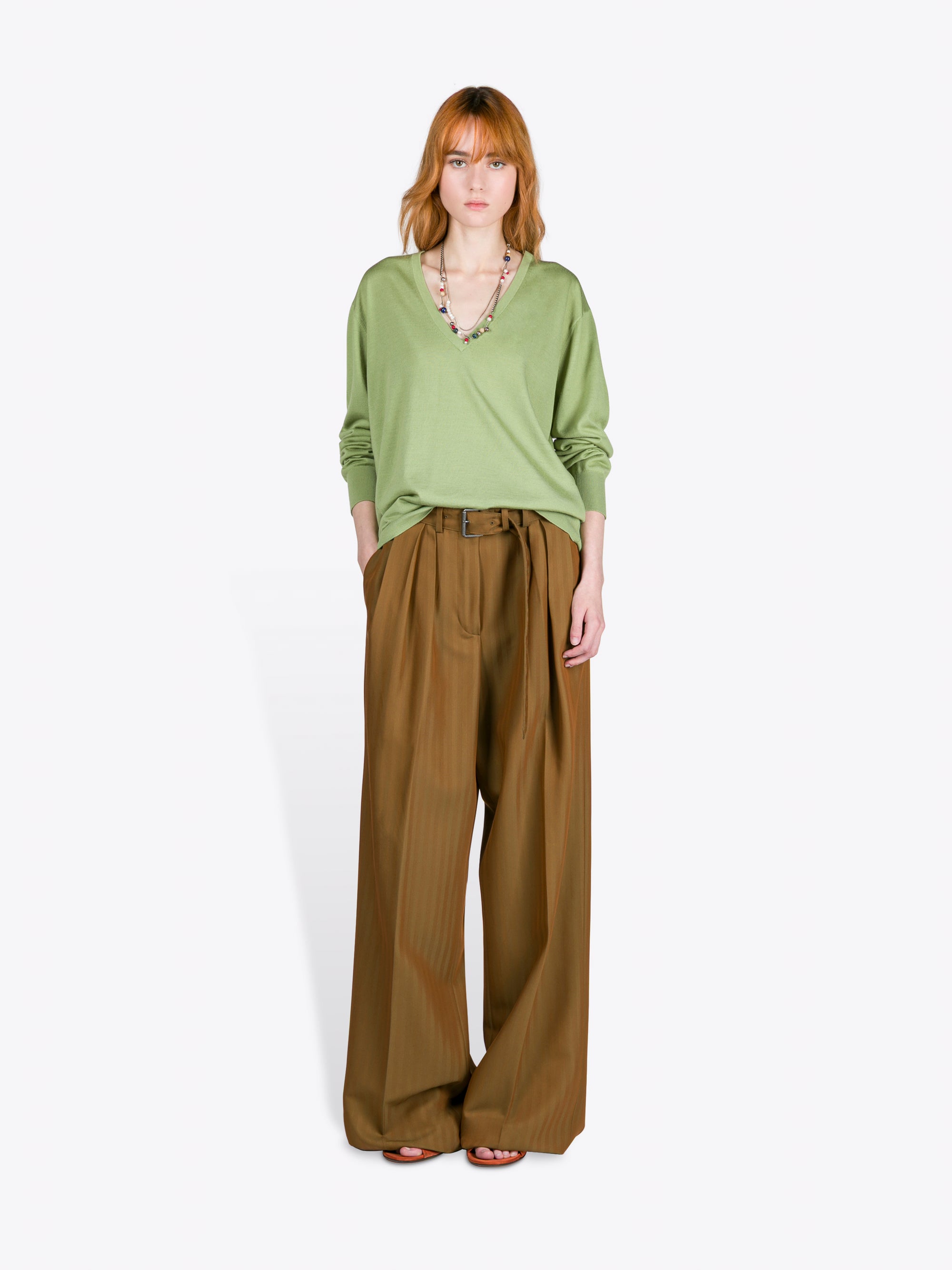 Woman wearing a green top and brown wide-leg pants on a white background