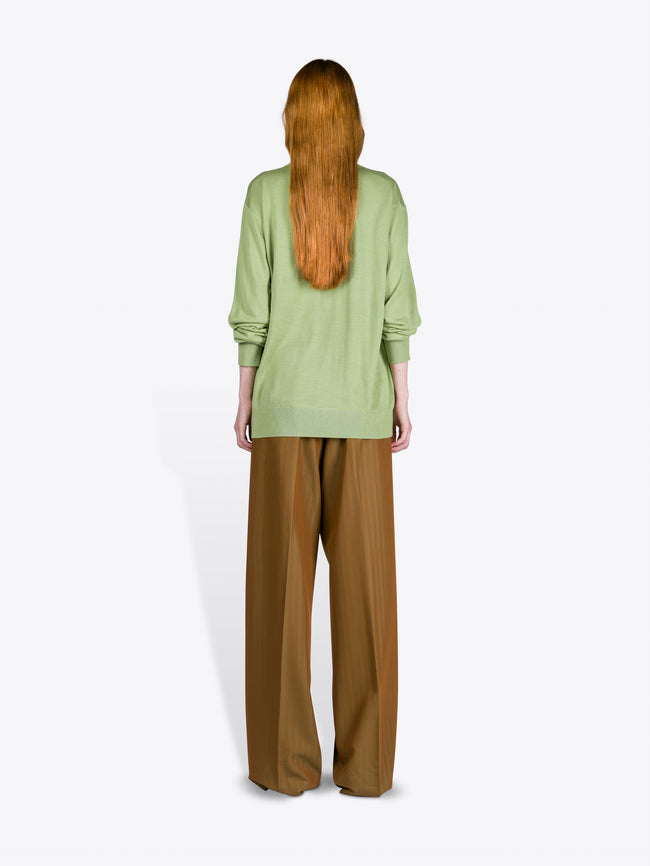 Person wearing a light green sweater and brown pants on a white background