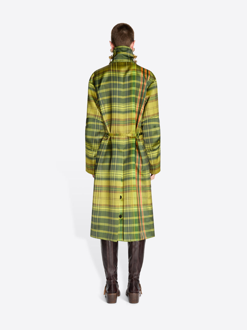 Back view of a model standing against a light gray background wearing a long green and yellow plaid coat with a high collar and waist tie and dark brown boots.