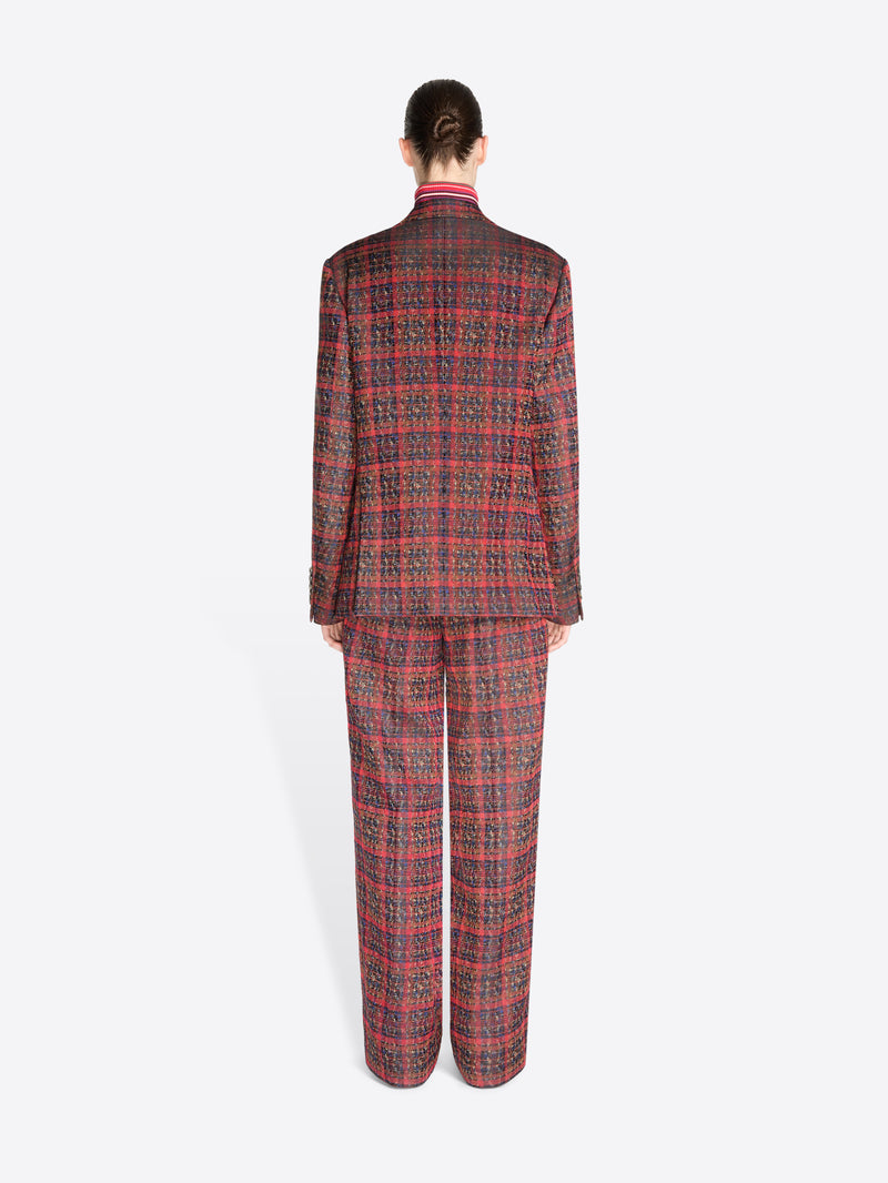 Back view of a model standing against a light gray background wearing a matching red and black plaid suit, featuring a double-breasted blazer and wide-leg pants, styled with a red striped turtleneck.