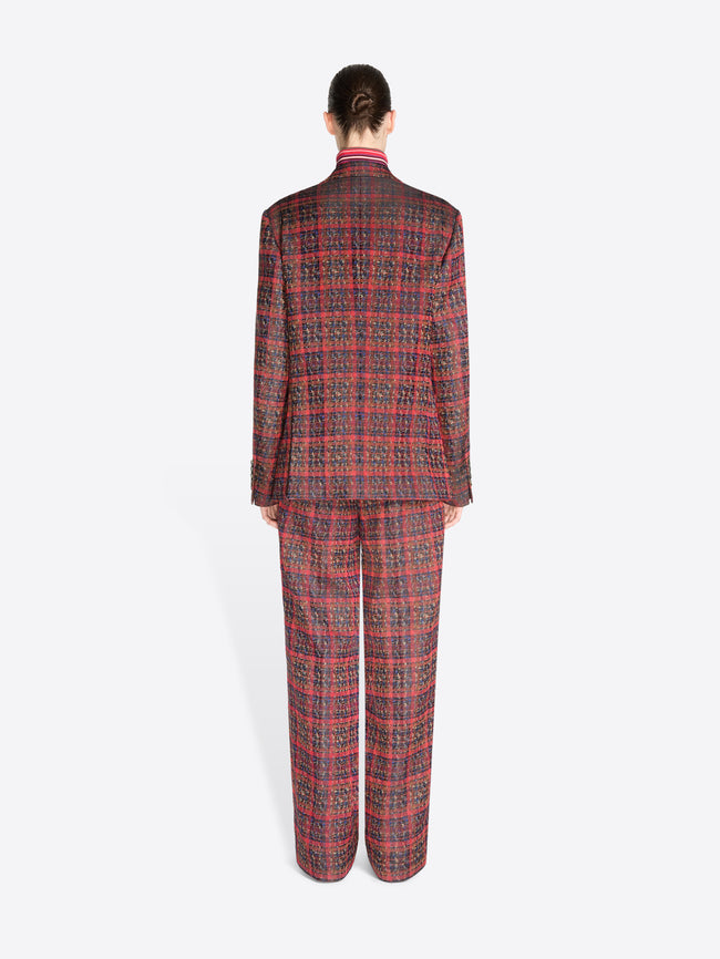 Back view of a model standing against a light gray background wearing a matching red and black plaid suit, featuring a double-breasted blazer and wide-leg pants, styled with a red striped turtleneck.