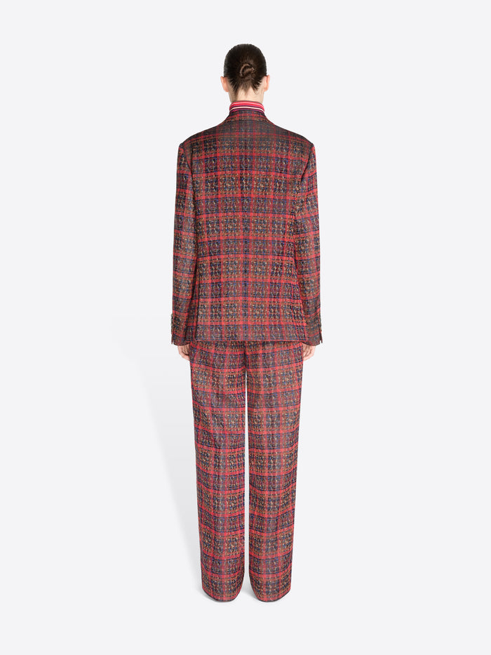 Back view of a model standing against a light gray background wearing a matching red and black plaid suit, featuring a double-breasted blazer and wide-leg pants, styled with a red striped turtleneck.