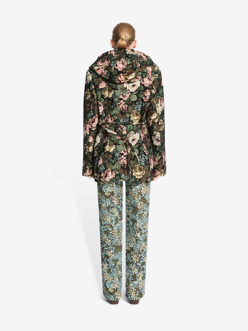Back view of a model standing against a light gray background wearing a dark floral-patterned coat, matching floral pants.