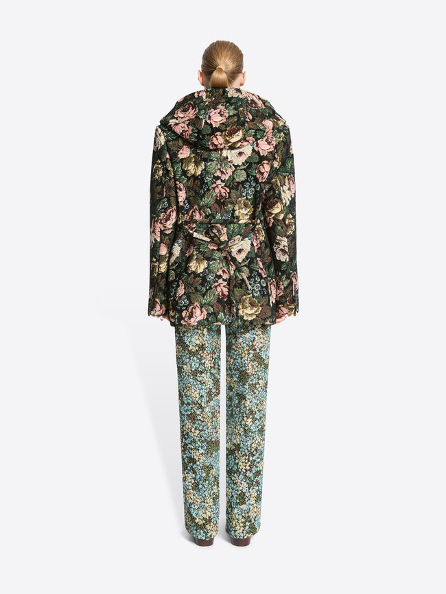 Back view of a model standing against a light gray background wearing a dark floral-patterned coat, matching floral pants.