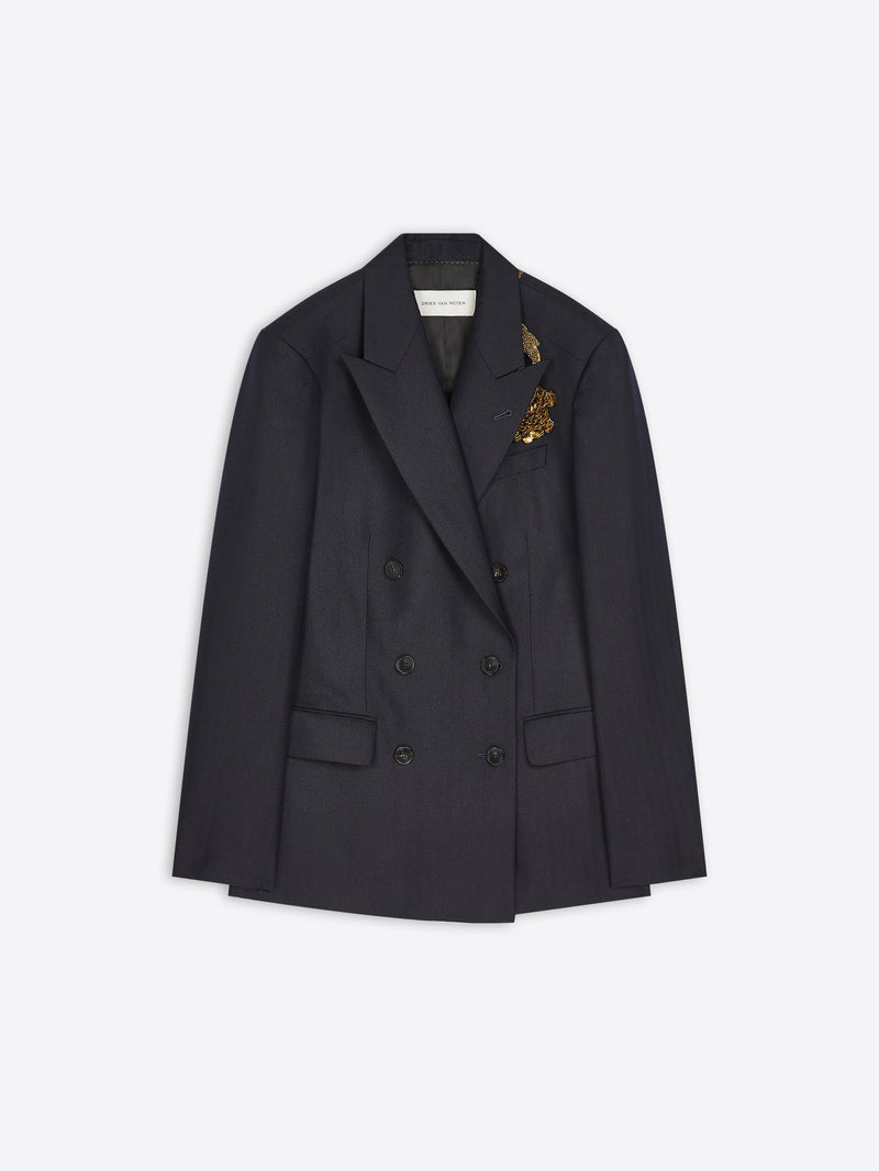 A dark double-breasted blazer with a small gold embroidered detail on the lapel, displayed flat against a light gray background.